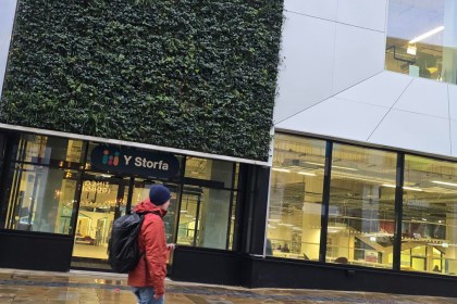 Exterior of Y Storfa showing vertical garden wall, glass windows, and entrance with pedestrian passing by.
