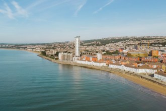 Coastal view of Swansea showing the beach, seafront buildings, the Meridian Tower and the city rising into the hills behind.
