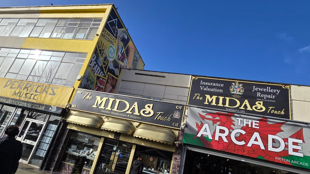 Street view of Derricks Music with its mural, The Midas Touch jewellery shop and the Picton Arcade entrance in Swansea city centre.