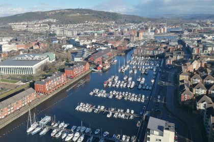 Aerial view of Swansea Marina with boats, waterfront apartments, the National Waterfront Museum and the city stretching towards the hills.