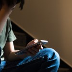 Teenager sitting on a staircase looking at a smartphone, appearing worried or overwhelmed, illustrating concerns about harmful online content.