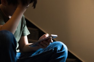 Teenager sitting on a staircase looking at a smartphone, appearing worried or overwhelmed, illustrating concerns about harmful online content.
