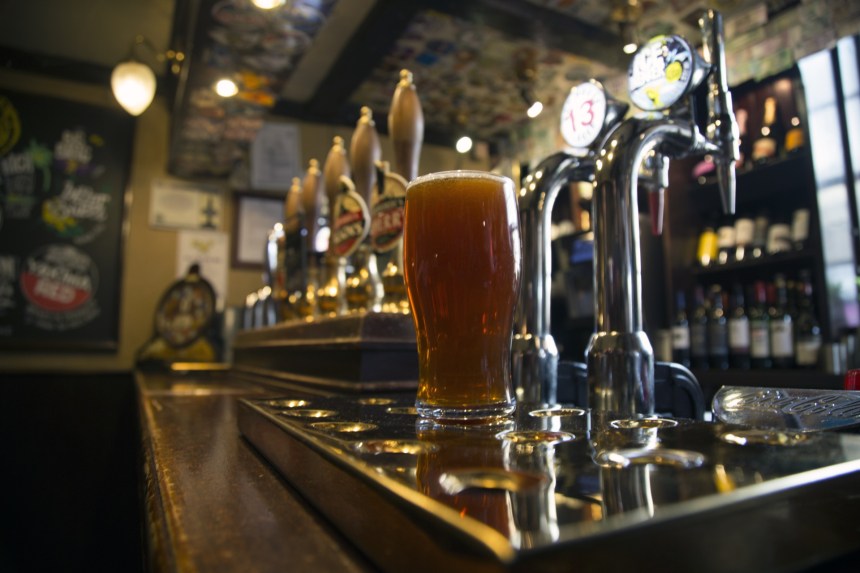 A pint of amber ale on the bar of a traditional pub, with beer taps and cask handles in the background.