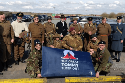Group of people dressed in historical military uniforms from different eras standing with The Great Tommy Sleep Out banner at Swansea Airport
