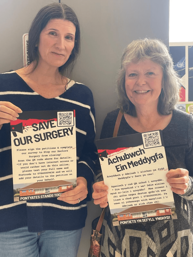 Clare Treharne and Jane Nicholas holding bilingual Save Our Surgery posters in Pontyates.