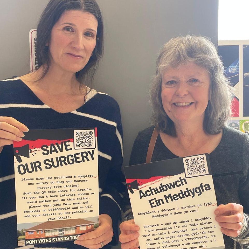 Clare Treharne and Jane Nicholas holding bilingual Save Our Surgery posters in Pontyates.