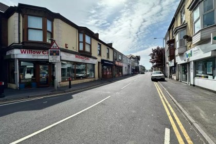 View along Station Road in Llanelli towards the railway station and level crossing, showing the Willow Café and local shops.