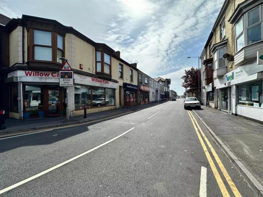 View along Station Road in Llanelli towards the railway station and level crossing, showing the Willow Café and local shops.