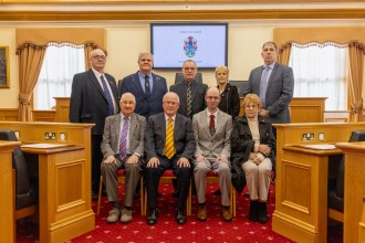 Independent councillors in the Llanelli Town Council chamber, seated and standing for a formal group photo. Leader Sean Rees is seated front row wearing a light grey suit and red tie.