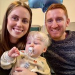Mother, father and young child with albinism sitting together on a sofa, smiling at the camera.