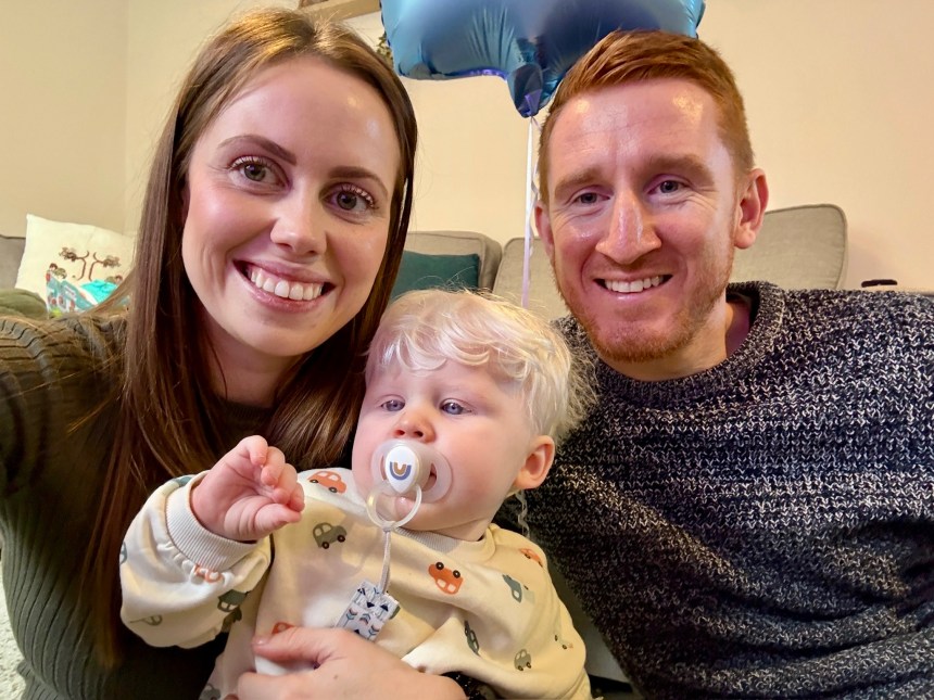 Mother, father and young child with albinism sitting together on a sofa, smiling at the camera.