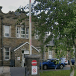 Exterior view of Maesteg Hospital showing stone façade, entrance porch, flagpole and parked cars in front.
