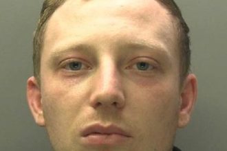 Police custody photograph of Thomas Morgan, a man in his late twenties with short brown hair wearing a black top