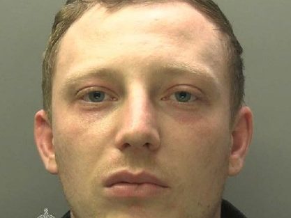 Police custody photograph of Thomas Morgan, a man in his late twenties with short brown hair wearing a black top