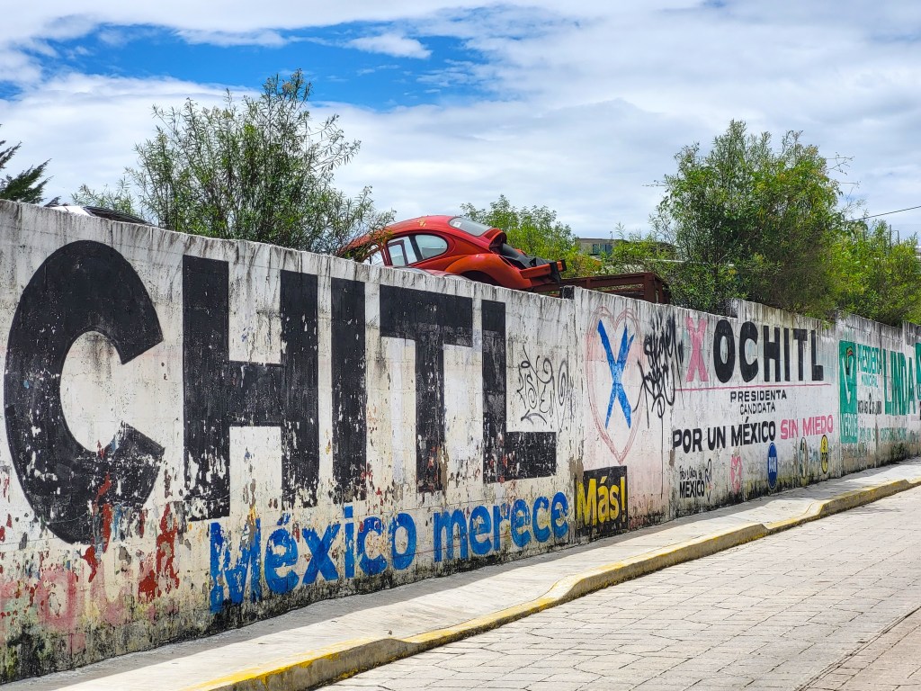 Red VW Beetle behind a painted political wall in Mexico.
