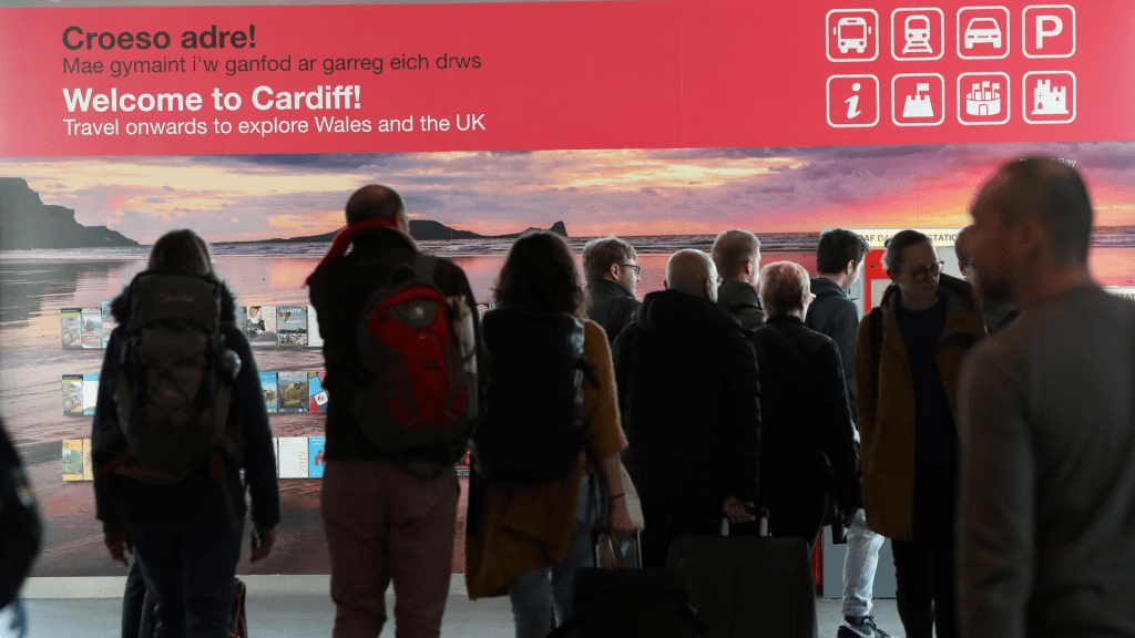Passengers walking through Cardiff Airport beneath a “Welcome to Cardiff” sign as French fans arrive for the Wales v France Six Nations match.