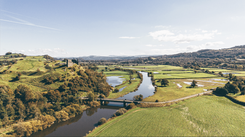 Aerial view of the River Tywi winding through green countryside with a bridge and historic castle ruins overlooking the valley in Carmarthenshire