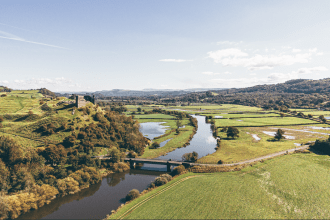 Aerial view of the River Tywi winding through green countryside with a bridge and historic castle ruins overlooking the valley in Carmarthenshire