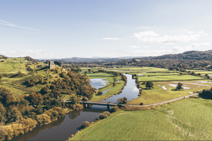 Aerial view of the River Tywi winding through green countryside with a bridge and historic castle ruins overlooking the valley in Carmarthenshire