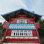 A photo of the ornate, red-painted Swiss Cottage in Singleton Park, showing its decorative balconies and inscriptions under a cloudy sky.