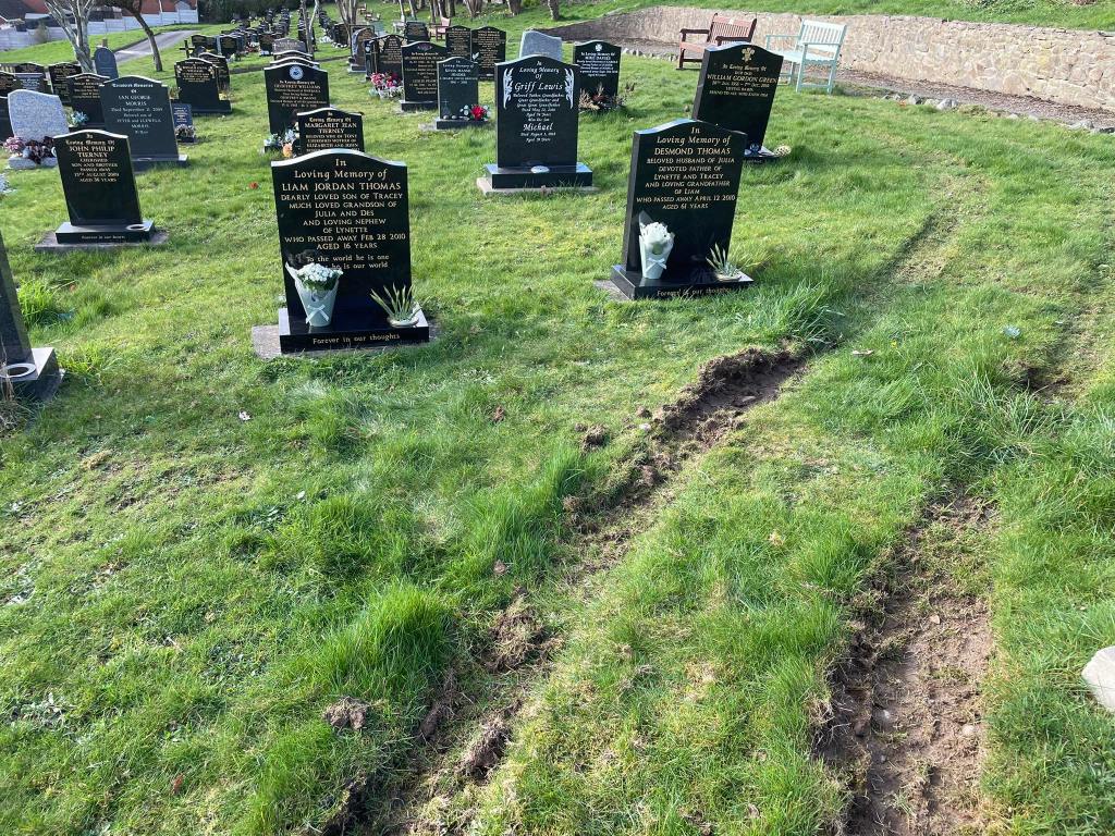 A photograph of Coedffranc Cemetery in Skewen showing deep muddy tyre tracks running across the grass between rows of headstones, passing close to the graves of Liam Jordan Thomas and Desmond Thomas.