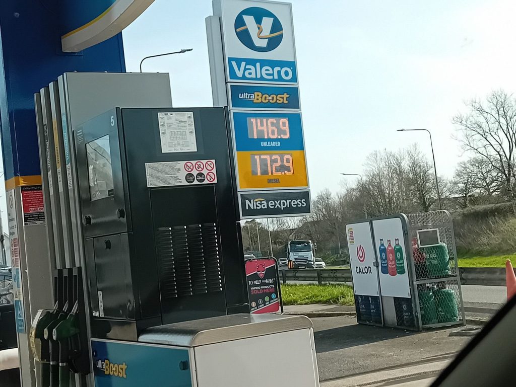 Price board at a Valero petrol station in St Clears showing unleaded at 146.9p per litre and diesel at 172.9p, with pumps and roadside visible under a clear sky.
