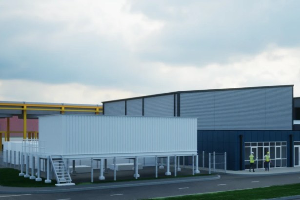 A sleek, modern industrial building with dark cladding and a large silver upper section, set in a clean, landscaped area with workers in high-visibility gear in the foreground. Bare trees and other industrial structures are visible in the background.