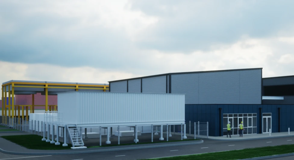 A sleek, modern industrial building with dark cladding and a large silver upper section, set in a clean, landscaped area with workers in high-visibility gear in the foreground. Bare trees and other industrial structures are visible in the background.