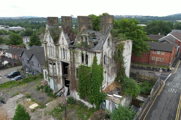 Aerial view of Danbert House in Morriston, Swansea, showing the dilapidated Victorian building with a damaged roof, broken windows and overgrown vegetation surrounding the structure.