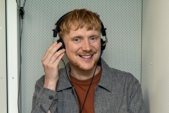 A man wearing headphones smiles while adjusting them during a hearing test inside a soundproof booth.