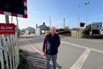 Carl Peters-Bond stands at a level crossing in St Clears near the proposed site of the reopened railway station.