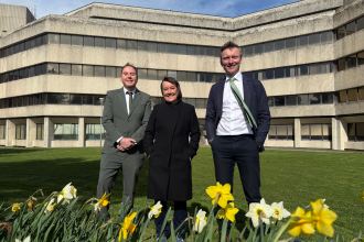 Torsten Bell MP, Welsh Secretary Jo Stevens and Swansea Council leader Rob Stewart stand outside Swansea Civic Centre with daffodils in the foreground after £20 million funding announcement.