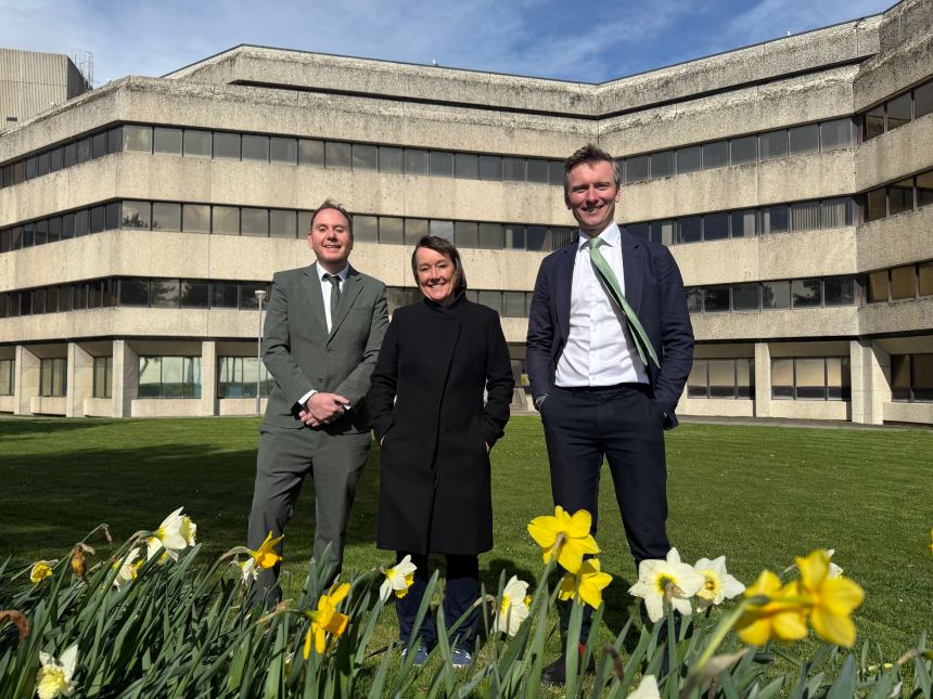 Torsten Bell MP, Welsh Secretary Jo Stevens and Swansea Council leader Rob Stewart stand outside Swansea Civic Centre with daffodils in the foreground after £20 million funding announcement.
