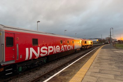 The red Railway 200 exhibition train Inspiration standing at a station platform at sunset.