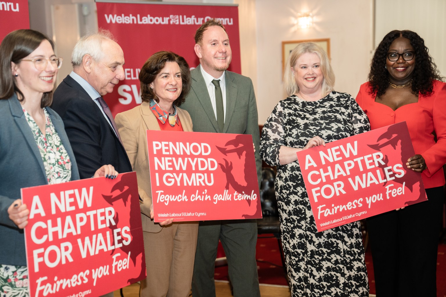A group of six people, including Eluned Morgan, Rob Stewart, and Mike Hedges, standing together on a stage smiling for a professional group photo.