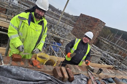 Two stonemasons in hi-vis jackets and hard hats lay bricks on scaffolding during restoration work on the Laboratory Building at the Hafod-Morfa Copperworks site in Swansea.