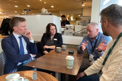 Swansea West MP Torsten Bell, wearing a suit and tie, sits at a cafe table with three other people, including M&S representatives, during an urgent meeting to discuss the closure of the city's Marks and Spencer store.
