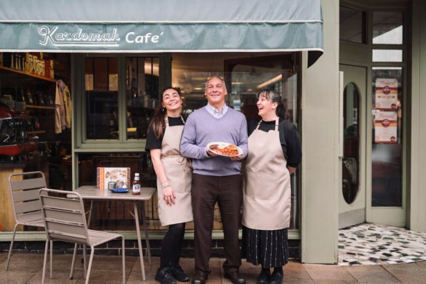 Three people stand outside Kardomah Cafe in Swansea, with owner Marcus Luporini holding a plate of breakfast food alongside two staff members wearing aprons at the café entrance.
