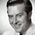 A black and white studio headshot of a smiling Ray Milland from the 1940s, wearing a white shirt and striped tie.