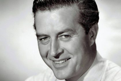 A black and white studio headshot of a smiling Ray Milland from the 1940s, wearing a white shirt and striped tie.