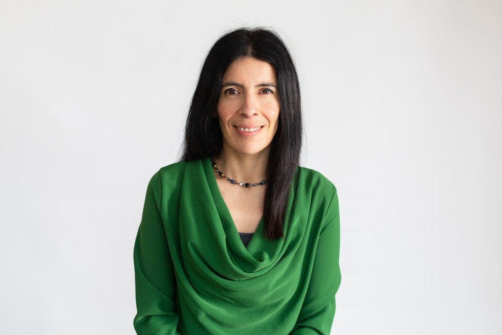 Rocio Cifuentes MBE, Children's Commissioner for Wales, smiling in a green cowl-neck top and a colourful beaded necklace against a plain white background.