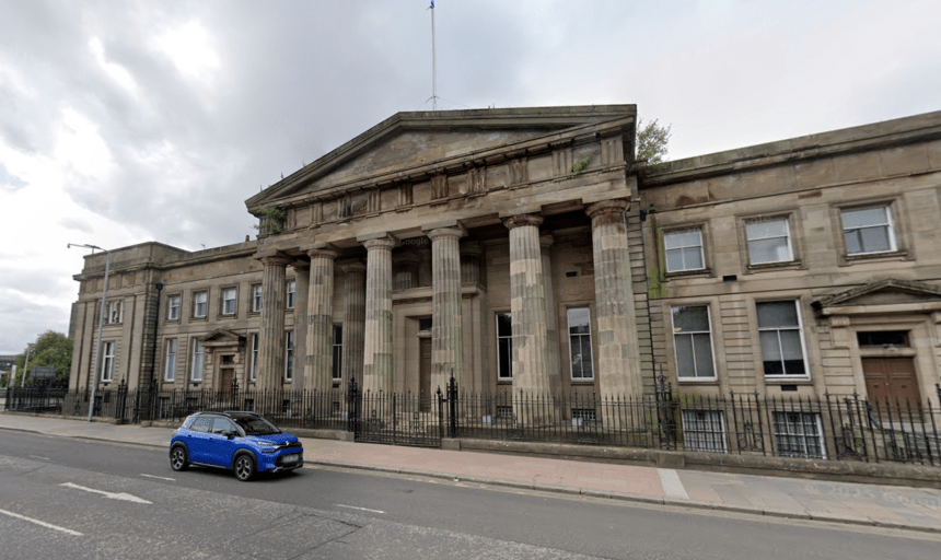 A street-level view of the historic High Court building in Glasgow, featuring large stone columns and a classical facade. A blue car is seen driving past on the road in the foreground under an overcast sky.