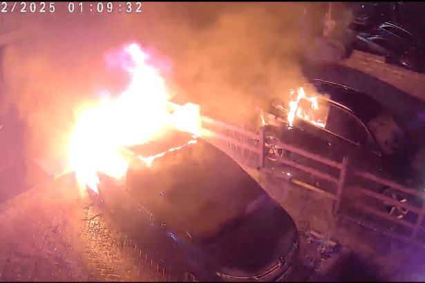 CCTV image showing a car on fire in a residential street in Brackla, Bridgend, with flames spreading to a nearby vehicle at night.