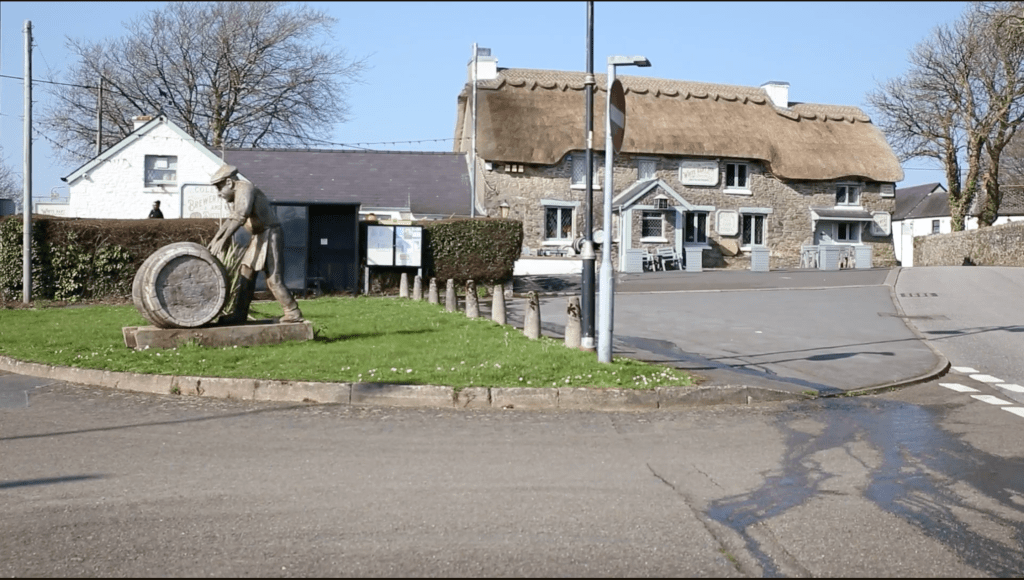 Exterior of the White Hart pub with thatched roof and statue outside in a village setting