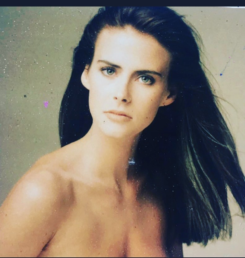 A vintage 1980s studio portrait of a young Annabel Schofield with long dark hair swept to one side, gazing directly into the camera with a composed, intense expression.