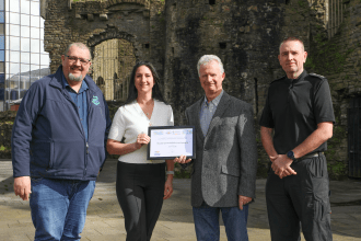 Four representatives from Swansea BID, Swansea Against Business Crime and South Wales Police holding a national safety accreditation certificate in Swansea city centre.