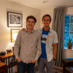 A portrait of two men, Tobias and Marc, standing in their living room. One has his arm around the other, and they are both smiling at the camera.