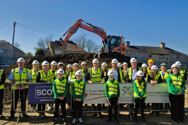 Group of pupils, council officials and construction workers in high-visibility jackets at a school building site with an excavator behind them in Townhill, Swansea.