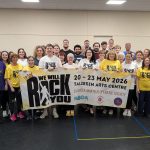 Group photo of SAOS members holding a banner for their 2026 production of We Will Rock You at the Taliesin Arts Centre.