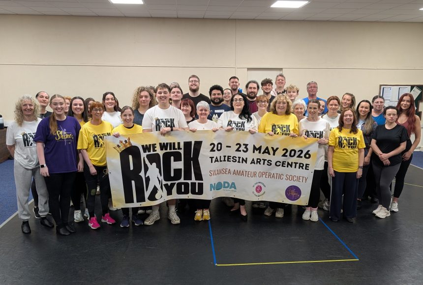 Group photo of SAOS members holding a banner for their 2026 production of We Will Rock You at the Taliesin Arts Centre.